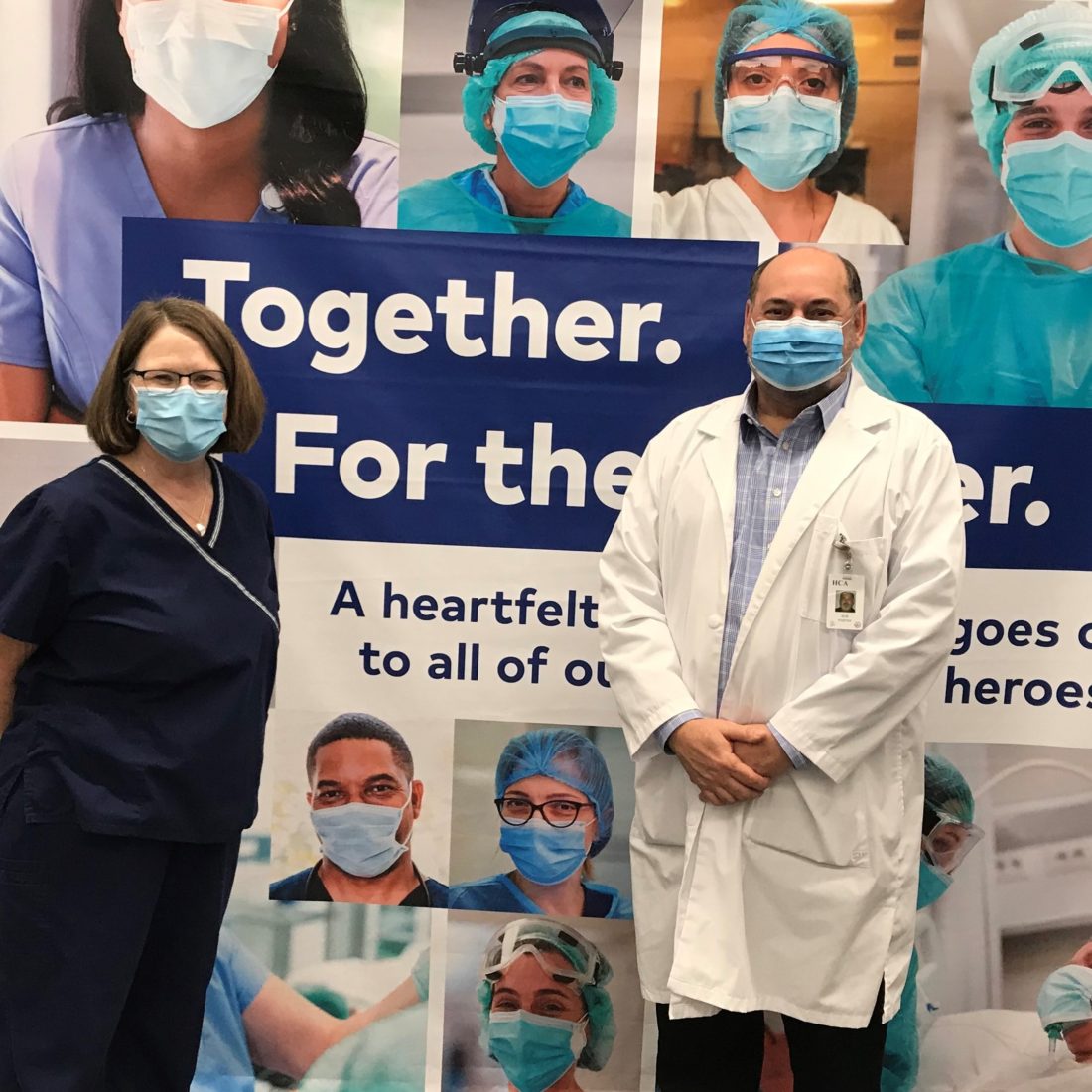 Man and woman wearing face masks posing in front of large backdrop with images of healthcare workers. 