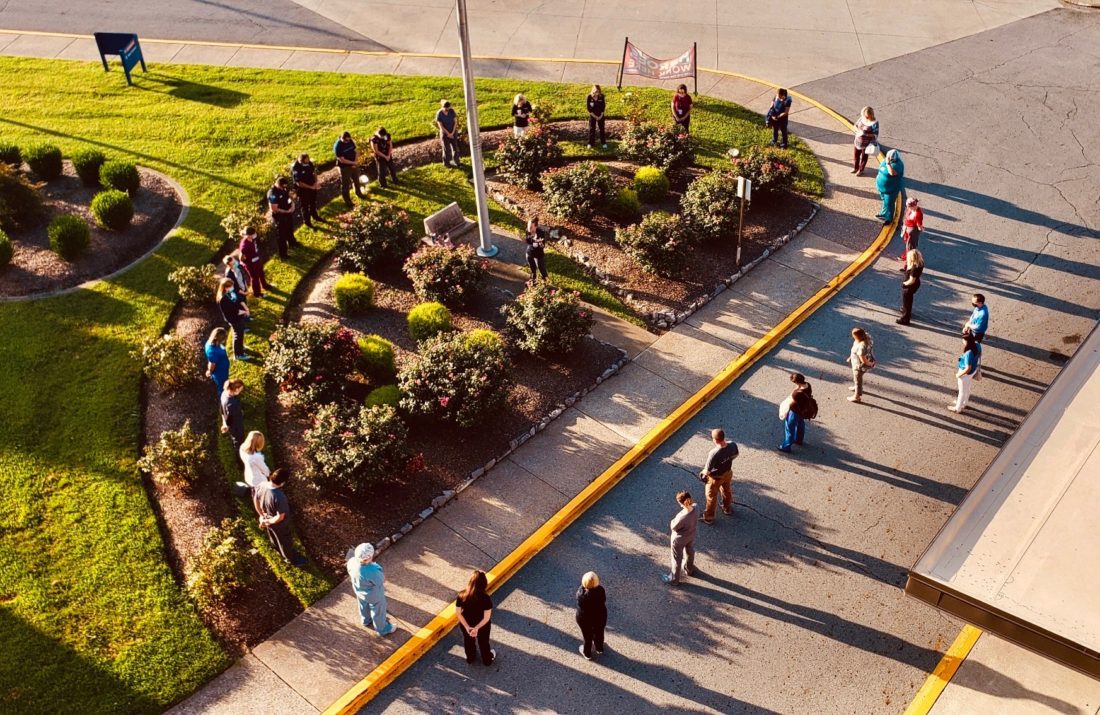 Aerial view of hospital workers standing in a circle around a flag pole. 