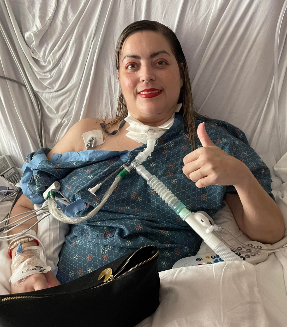 A woman in a hospital bed giving a thumbs up sign