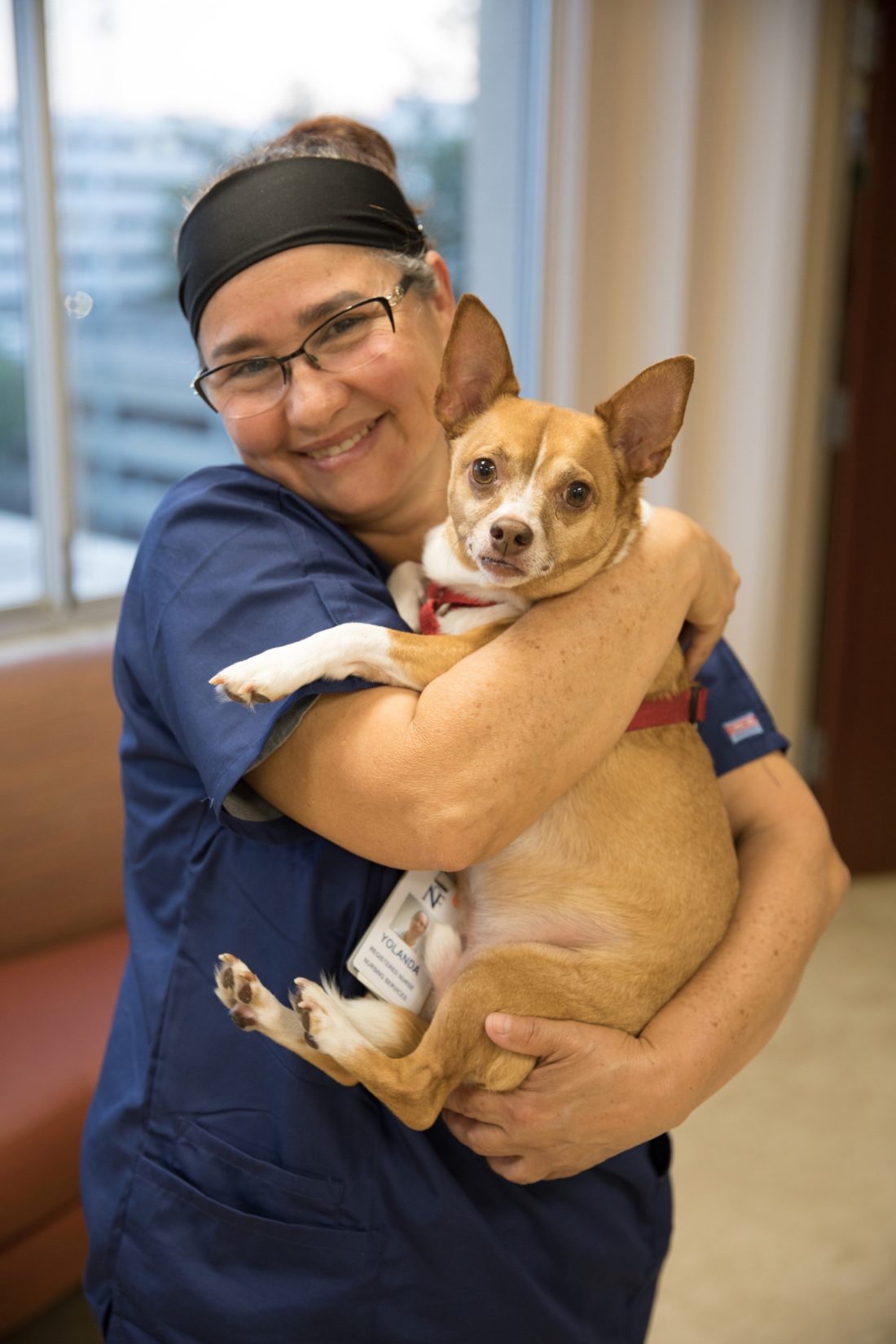 A nurse smiling for a picture while holding a small dog 