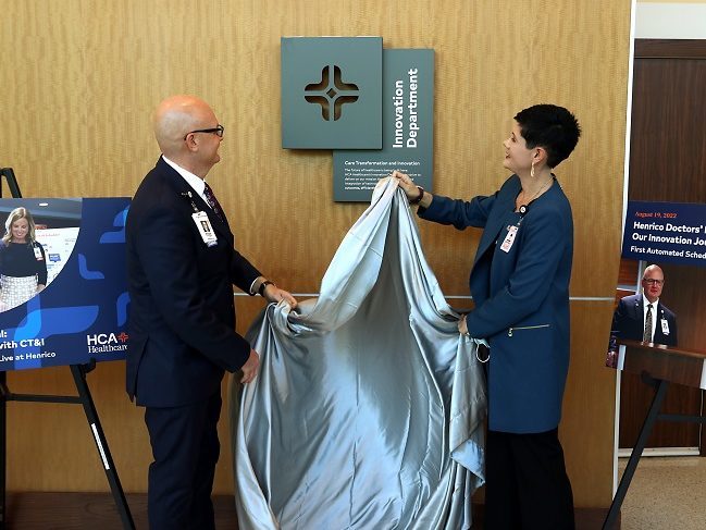 Whitney Staub-Juergens and Ryan Jensen unveiling a sign that reads "Innovation Department" at a Virginia hospital. 