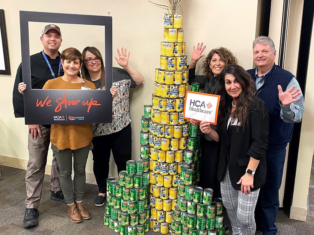 HCA Healthcare colleagues smiling for photo near canned corn in the shape of a large corn stalk.