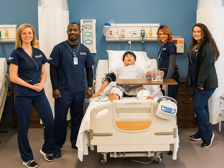 Four nursing students standing in a training hospital room.
