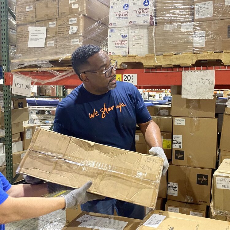 HCA Healthcare colleague in a 'We Show Up' shirt sorting boxes in a warehouse. 
