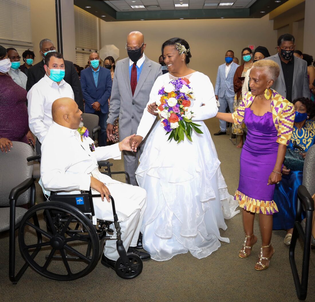 HCA Healthcare stroke patient in a wheelchair holding the hand of his bride at a hospital wedding ceremony. 